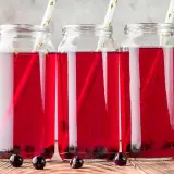 Tre glasflaskor med aroniajuice och sugrör. Perfekt för ett aronia recept.
