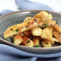 Grillad palsternacka i en krämig sås med örter, serverad i en grå skål på en blå duk.