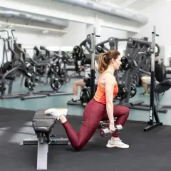 Kvinna utför bulgarian split squat med hantlar, tränar benmuskler och rumpa i gym.