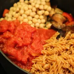 En proteinrik matlåda recept med pasta, kikärtor, tomatsås och grönsaker i en gjutjärnspanna.
