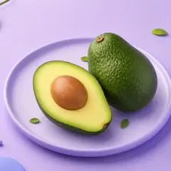 En hel och en halv avokado på en lila tallrik. En grön kvist med blad och lila kulor dekorerar bakgrunden. Avokado kalorier är bra att känna till för en hälsosam kost.