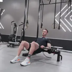 Man utför höftlyft med skivstång för att bygga muskler i rumpan. Träningspasset sker i ett modernt gym.