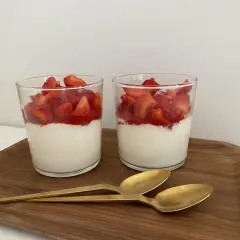 Två glas med grädde och färska jordgubbar, en läcker dessert som passar även för diabetiker typ 2. Två guldfärgade skedar ligger på en träbricka.