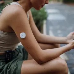 Kvinna med glukosmätare på armen och mobil i handen, som visar hur tekniken kan hjälpa vid prediabetes kost.