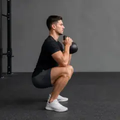 Man utför en goblet squat med en kettlebell framför bröstet i ett gym.