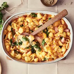 En krämig pastarätt med lax och spenat, perfekt för nyttiga recept. En träsked lyfter upp en portion ur ugnsformen.