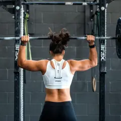 Stark kvinna lyfter skivstång över huvudet i ett gym. Hennes ryggmuskler syns tydligt. Ett perfekt pass för att bygga styrka.