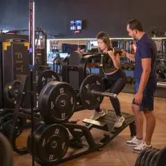 Kvinna utför benpress med instruktör vid sin sida, en del av ett push pull program.