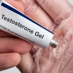 En hand håller en tub med testosterongel. Frågan "hur får man mer testosteron" kan besvaras med denna typ av behandling.