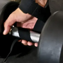 En hand med dragremmar gym greppar ett tungt hantelhandtag för ett stadigt lyft.