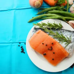 Laxfilé med rosmarin och pepparkorn, omgiven av grönsaker som morötter, haricots verts och vitlök. Perfekt d-vitamin mat för en hälsosam måltid.