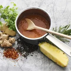 En kastrull med en läcker, **kalorisnål sås** omgiven av färsk ingefära, ananas, pepparkorn och chiliflakes.