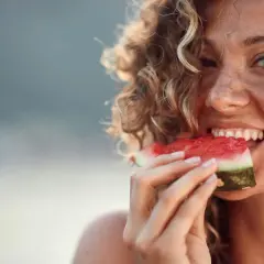 En kvinna med lockigt hår njuter av en saftig bit vattenmelon, ett bevis på att vattenmelon nyttigt är sant.