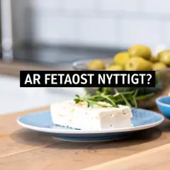 En bit fetaost på en blå tallrik, med oliver och olivolja i bakgrunden. Frågan "Är fetaost nyttigt?" visas i text.