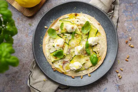 En läcker plattbrödpizza med zucchini, mozzarella och pinjenötter. Perfekt som ett snabbt mellanmål att ta med.