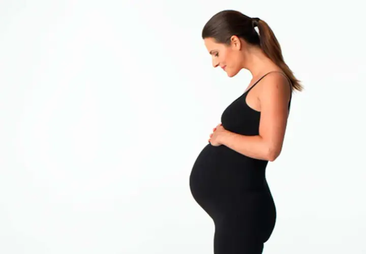Gravid kvinna i svart klänning håller om sin mage. Hon ser kärleksfullt ner på sin honung.