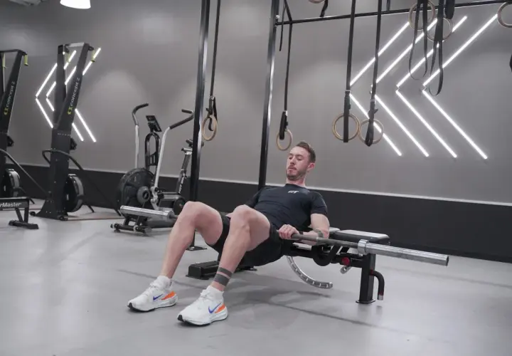 Man utför höftlyft med skivstång för att bygga muskler i rumpan. Träningspasset sker i ett modernt gym.