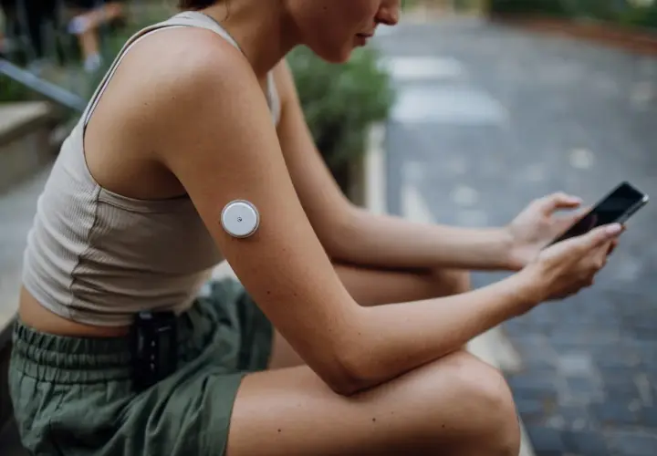 Kvinna med glukosmätare på armen och mobil i handen, som visar hur tekniken kan hjälpa vid prediabetes kost.