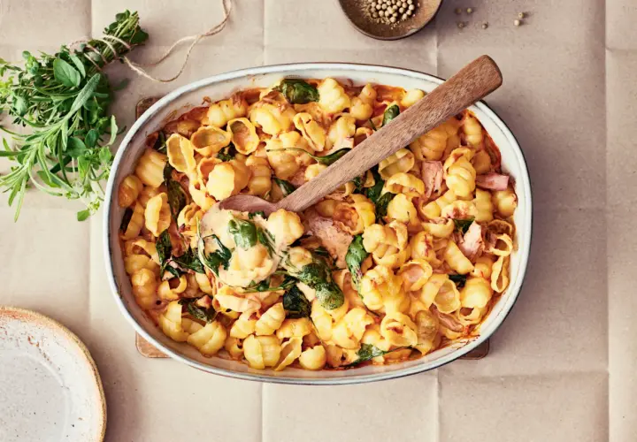 En krämig pastarätt med lax och spenat, perfekt för nyttiga recept. En träsked lyfter upp en portion ur ugnsformen.