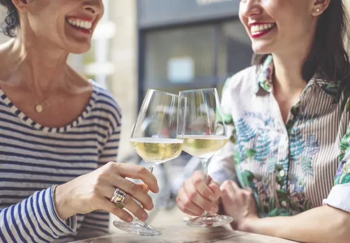 Två glada kvinnor skålar med vitt vin. En titt på kalorier alkohol tabell kan vara bra att ha i åtanke.