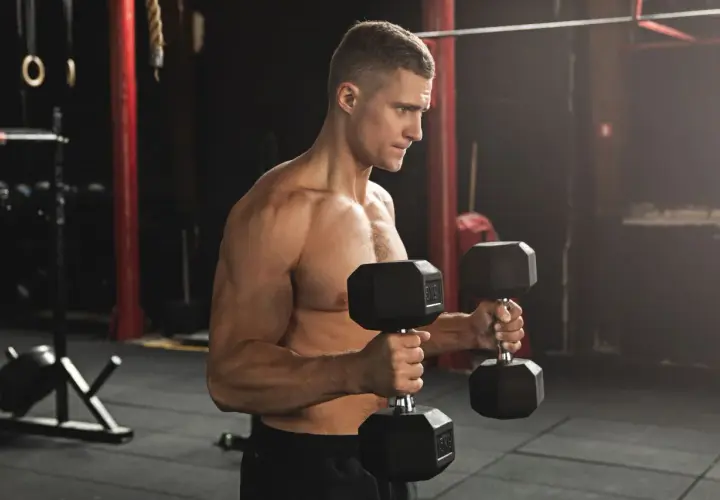 Man utför hammercurls med hantlar i ett gym.