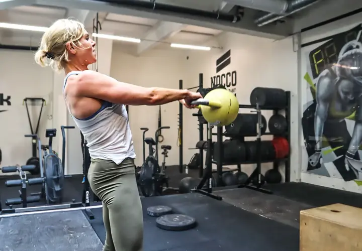 Stark kvinna utför en kettlebell thruster i ett gym.