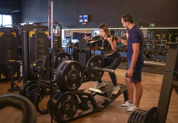Kvinna utför benpress med instruktör vid sin sida, en del av ett push pull program.