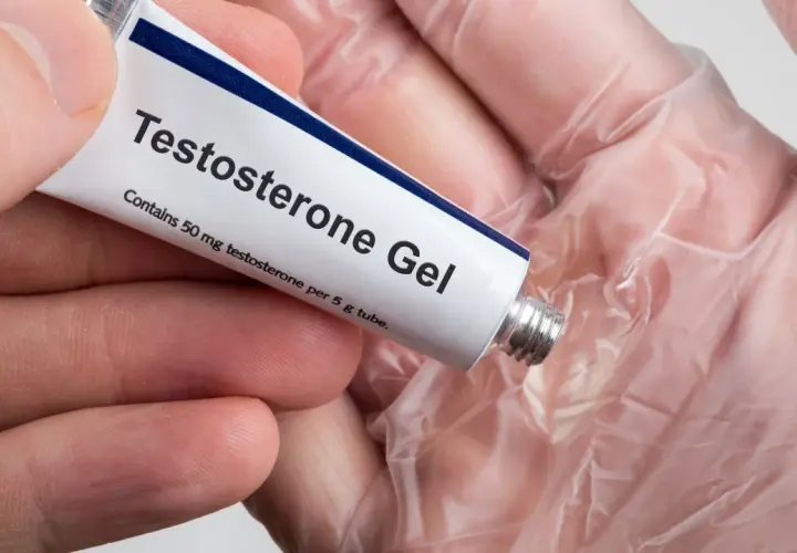 En hand håller en tub med testosterongel. Frågan "hur får man mer testosteron" kan besvaras med denna typ av behandling.