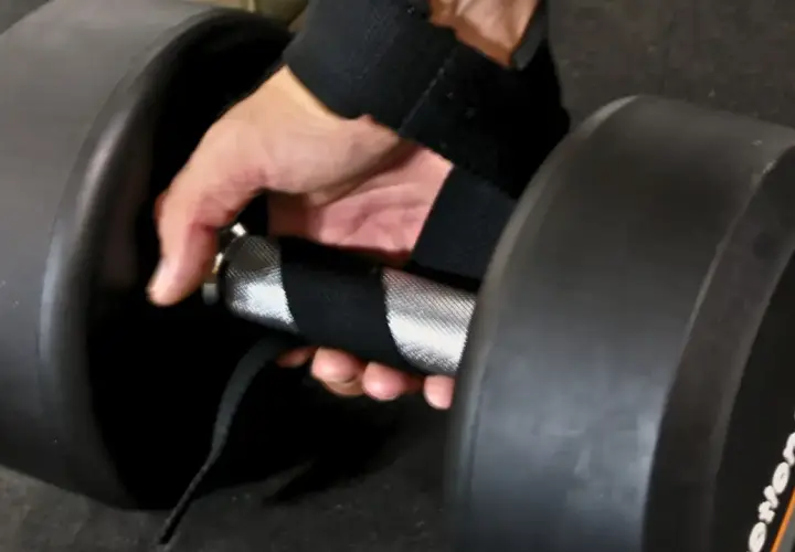 En hand med dragremmar gym greppar ett tungt hantelhandtag för ett stadigt lyft.