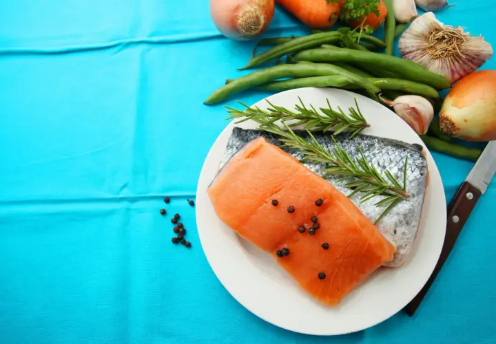 Laxfilé med rosmarin och pepparkorn, omgiven av grönsaker som morötter, haricots verts och vitlök. Perfekt d-vitamin mat för en hälsosam måltid.