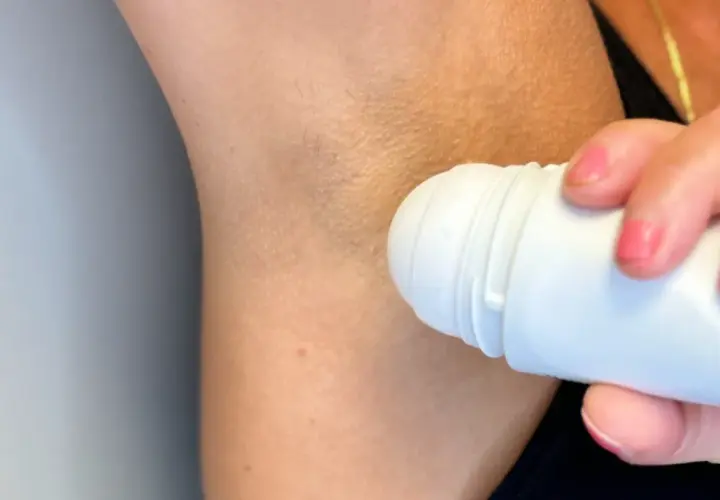 En person applicerar roll-on deodorant under armen. Trots deodoranten kan det ibland lukta svett.