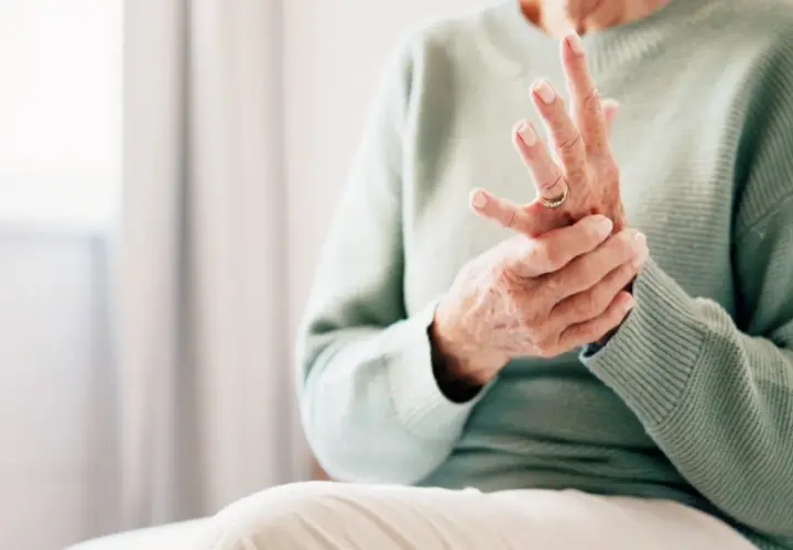 Äldre person som håller sin hand, fingrarna böjda, möjligen på grund av kronisk inflammation.