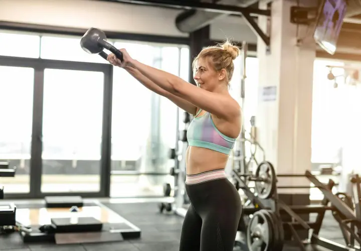 Kvinna utför kettlebell-svängar i gymmet. Bra gymtips för en helkroppsträning.