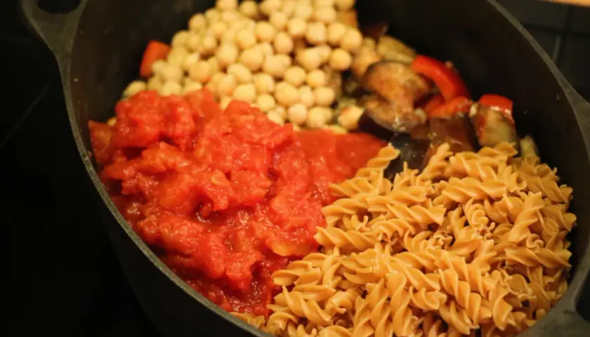 En proteinrik matlåda recept med pasta, kikärtor, tomatsås och grönsaker i en gjutjärnspanna.