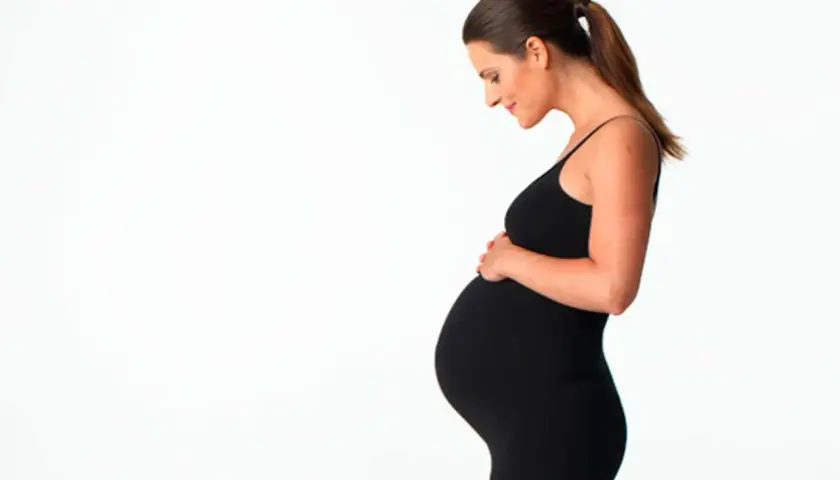 Gravid kvinna i svart klänning håller om sin mage. Hon ser kärleksfullt ner på sin honung.