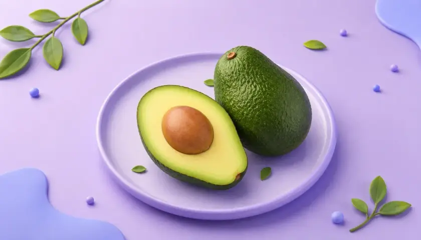En hel och en halv avokado på en lila tallrik. En grön kvist med blad och lila kulor dekorerar bakgrunden. Avokado kalorier är bra att känna till för en hälsosam kost.