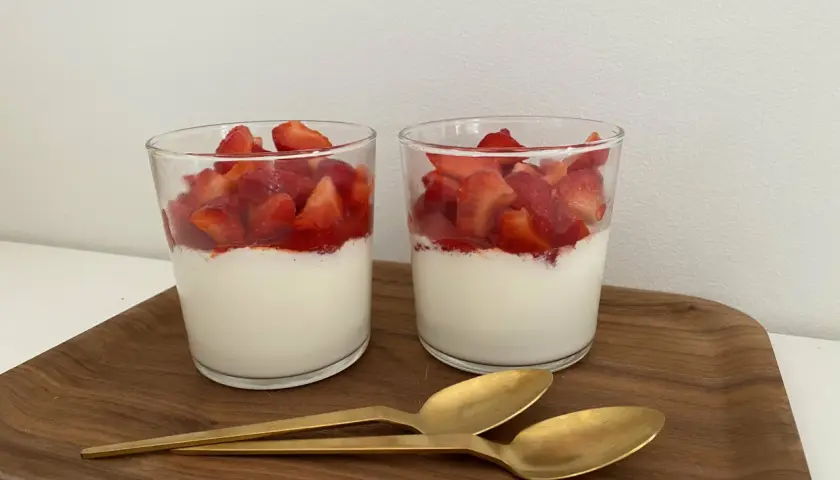 Två glas med grädde och färska jordgubbar, en läcker dessert som passar även för diabetiker typ 2. Två guldfärgade skedar ligger på en träbricka.