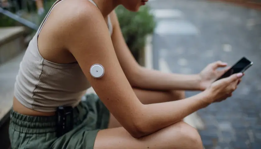 Kvinna med glukosmätare på armen och mobil i handen, som visar hur tekniken kan hjälpa vid prediabetes kost.