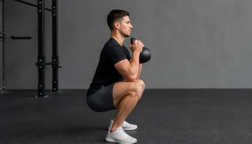 Man utför en goblet squat med en kettlebell framför bröstet i ett gym.