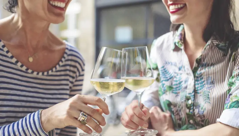 Två glada kvinnor skålar med vitt vin. En titt på kalorier alkohol tabell kan vara bra att ha i åtanke.