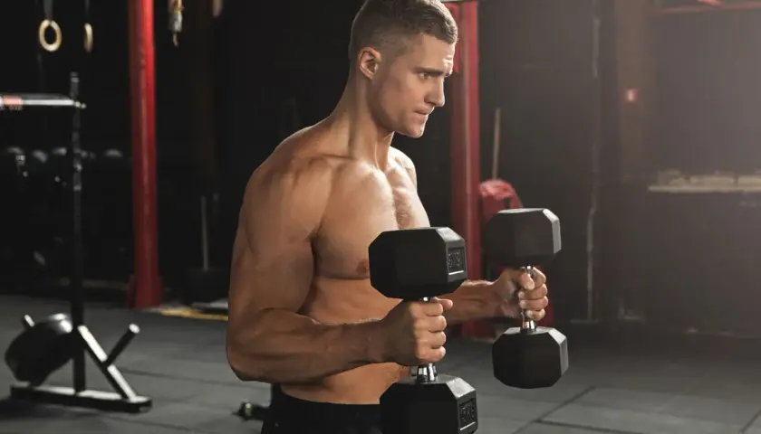 Man utför hammercurls med hantlar i ett gym.