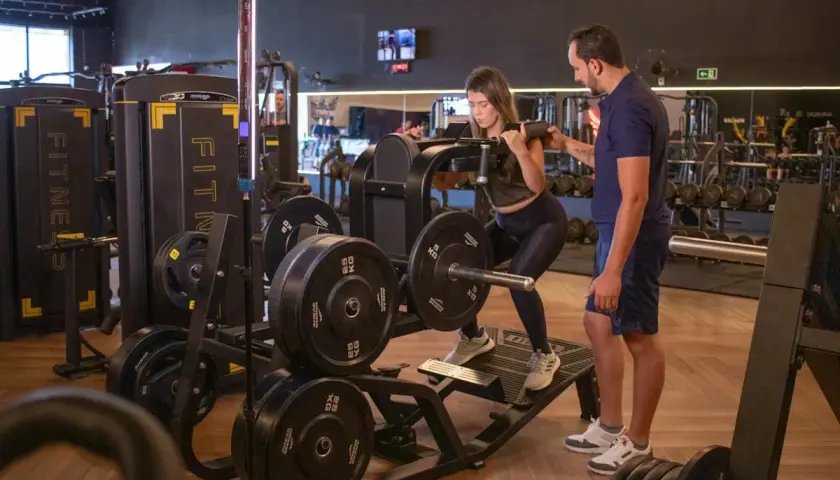 Kvinna utför benpress med instruktör vid sin sida, en del av ett push pull program.