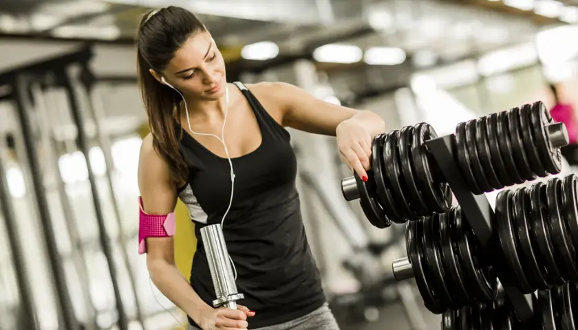 En kvinna väljer vikter på gymmet för sina reps och set.