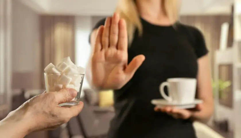 En person nekar sockerbitar och en kopp kaffe, en symbol för att sluta med socker och undvika biverkningar.