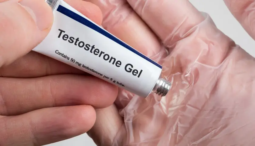 En hand håller en tub med testosterongel. Frågan "hur får man mer testosteron" kan besvaras med denna typ av behandling.