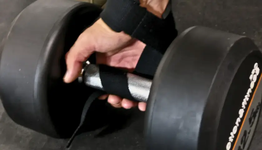En hand med dragremmar gym greppar ett tungt hantelhandtag för ett stadigt lyft.