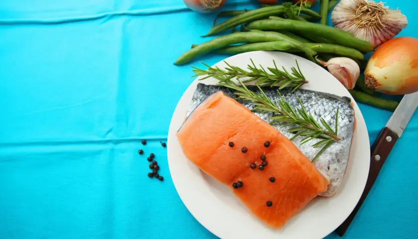 Laxfilé med rosmarin och pepparkorn, omgiven av grönsaker som morötter, haricots verts och vitlök. Perfekt d-vitamin mat för en hälsosam måltid.