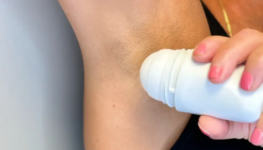 En person applicerar roll-on deodorant under armen. Trots deodoranten kan det ibland lukta svett.