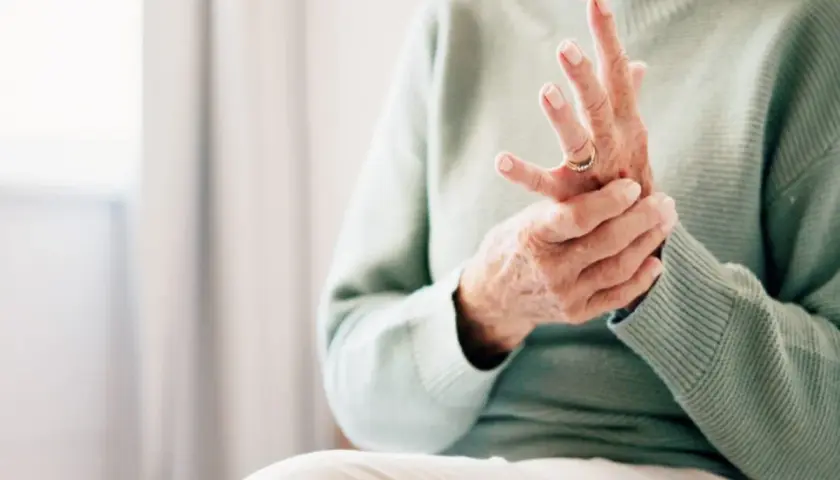 Äldre person som håller sin hand, fingrarna böjda, möjligen på grund av kronisk inflammation.
