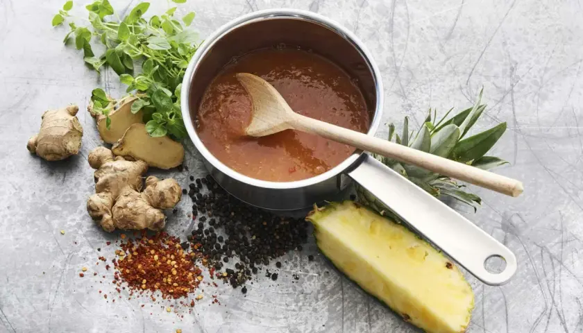 En kastrull med en läcker, **kalorisnål sås** omgiven av färsk ingefära, ananas, pepparkorn och chiliflakes.
